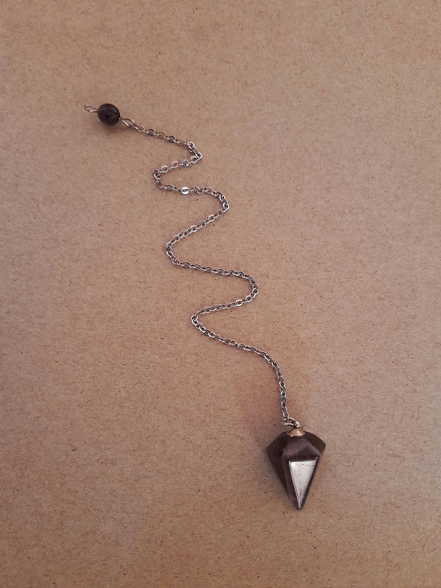 A picture of a silver dowsing pendulum on sand